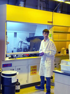 A white student in a lab coat standing in a chemistry lab